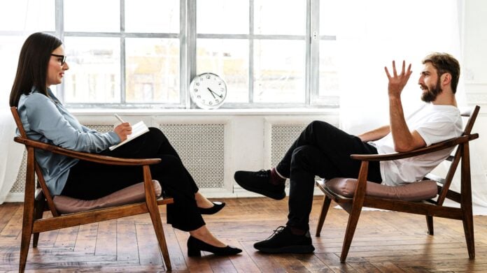 Person in Black Pants and Black Shoes Sitting on Brown Wooden Chair By Cottonbro