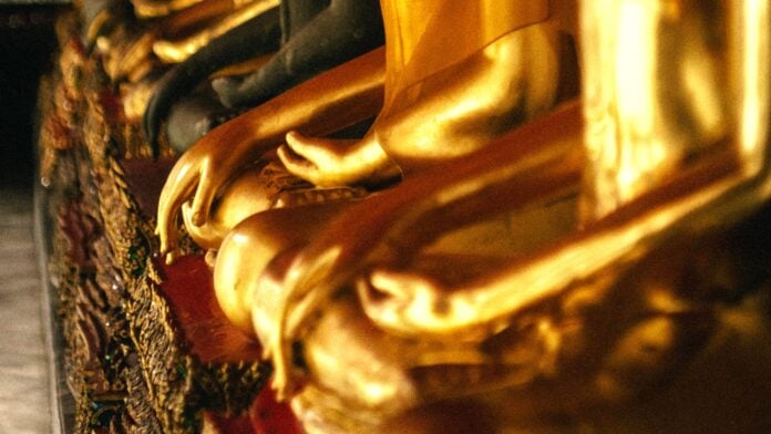 A row of gold Buddha statues in the morning sunrise By Ilya Batorshin