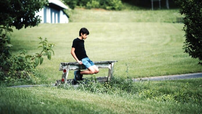 Boy sitting on a farm bench in green pasture By Tolga Ahmetler