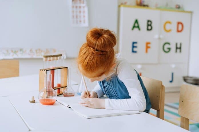 Girl Writing in a notebook at a school desk by Mikhail Nilov