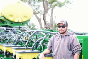 Alex Millershaski stands next to a seed planter used for crops like wheat, corn and sorghum.