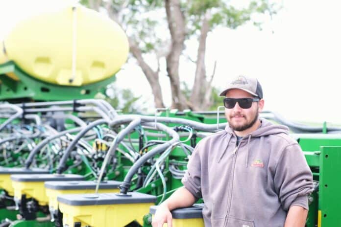 Alex Millershaski stands next to a seed planter used for crops like wheat, corn and sorghum.